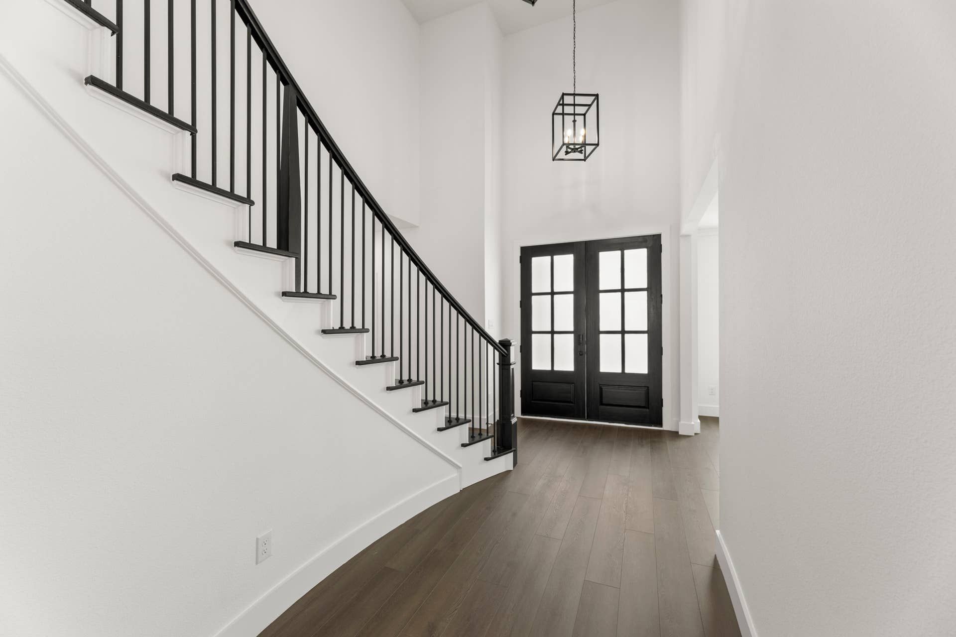 Modern entryway with dark wood flooring, black staircase, and double front doors.