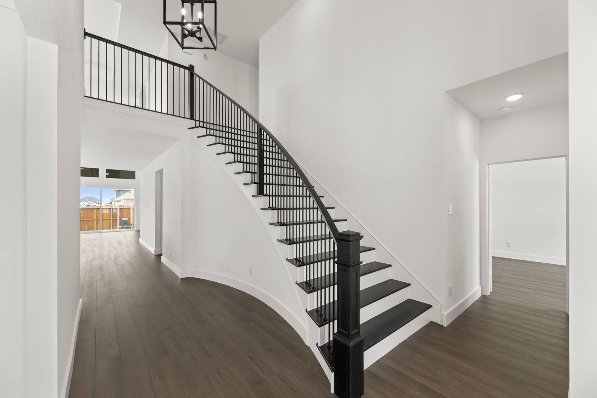 Elegant entryway with curved staircase and modern chandelier in a spacious interior.