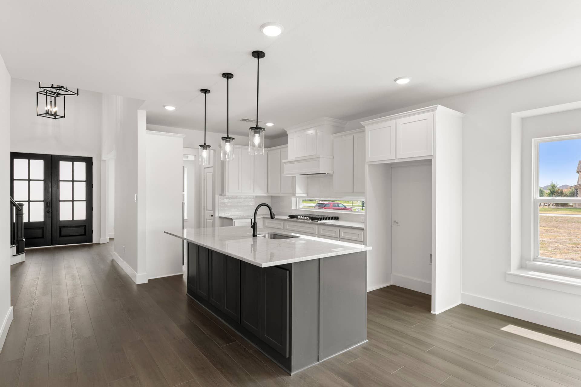 Modern kitchen with marble island, pendant lights, and dark wood flooring.