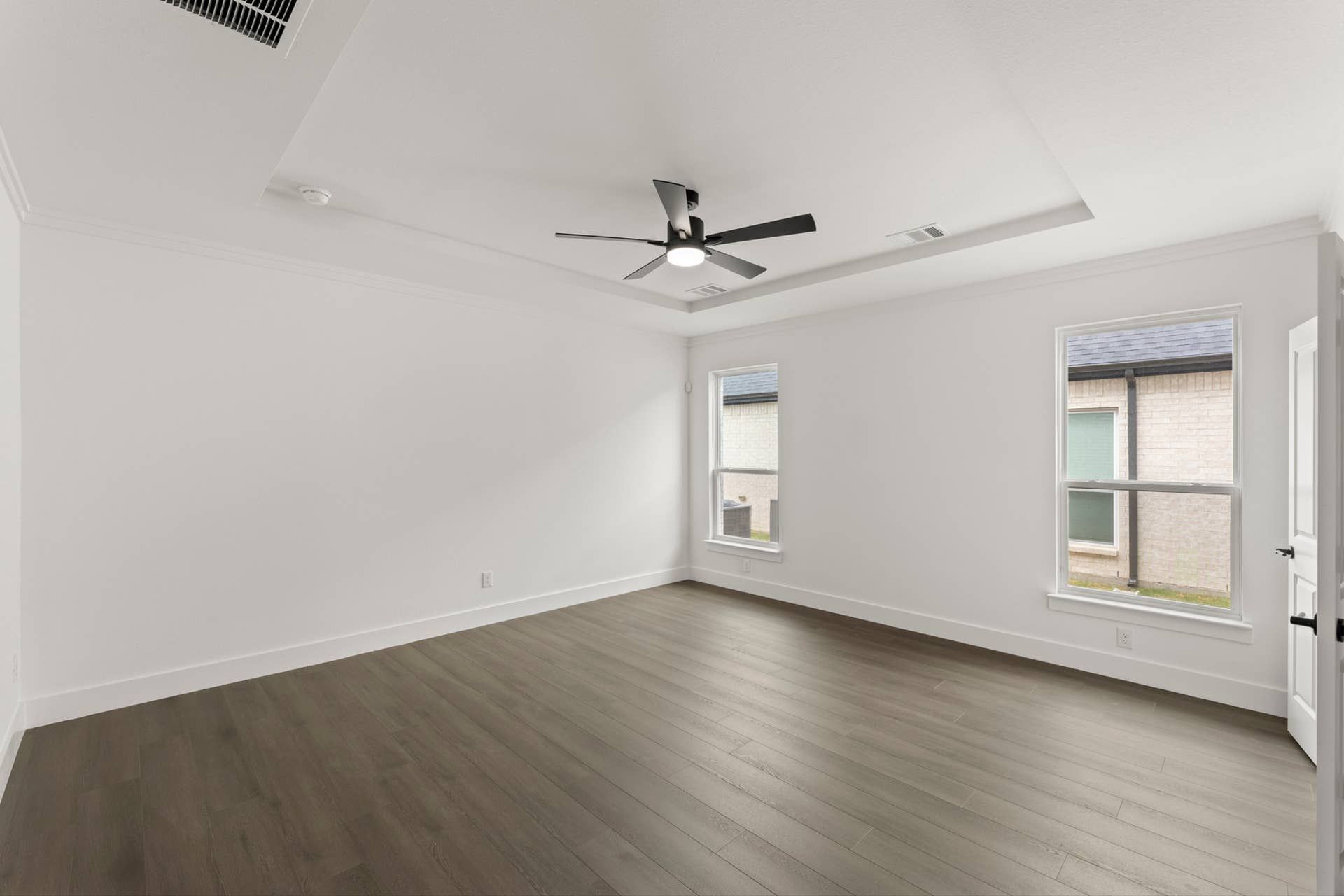 Spacious bedroom with wood flooring, ceiling fan, and natural light from large windows.