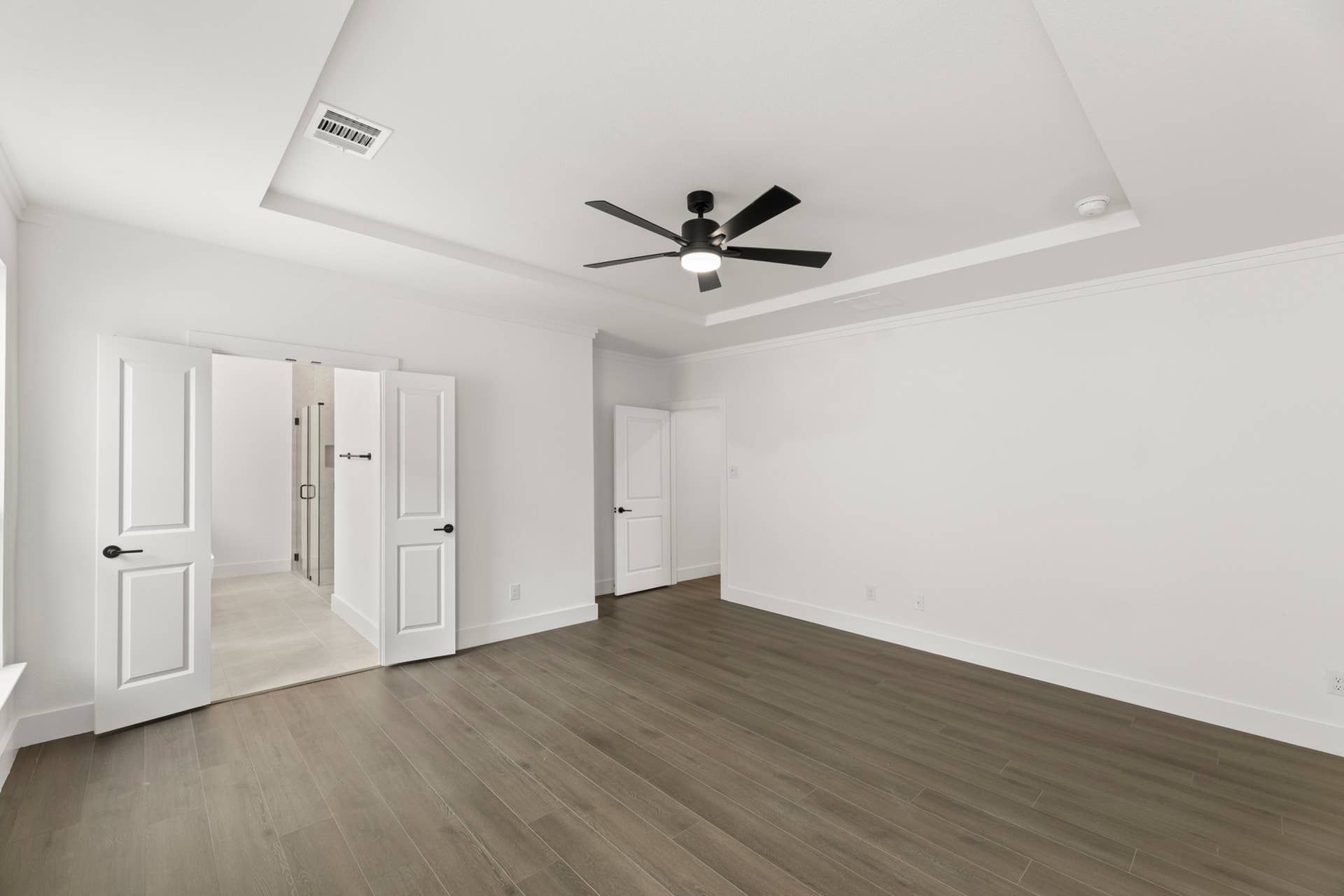 Spacious modern bedroom with wooden floors and ceiling fan, leading to ensuite bathroom.