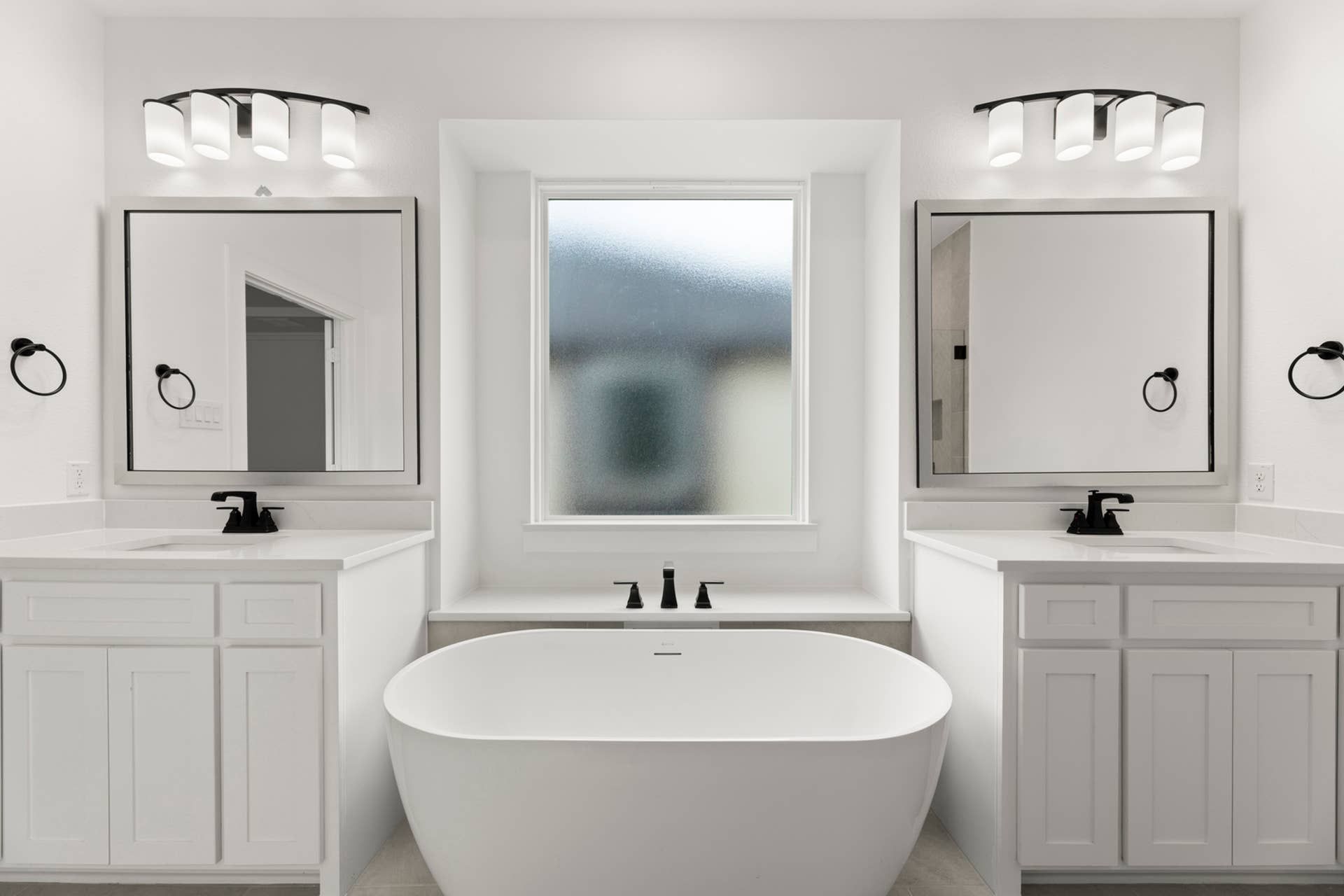 Modern bathroom with freestanding tub, dual vanities, and large frosted window.