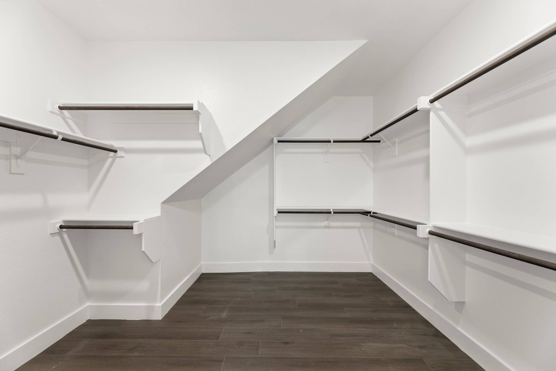 Spacious walk-in closet with dark wood flooring and white shelving.