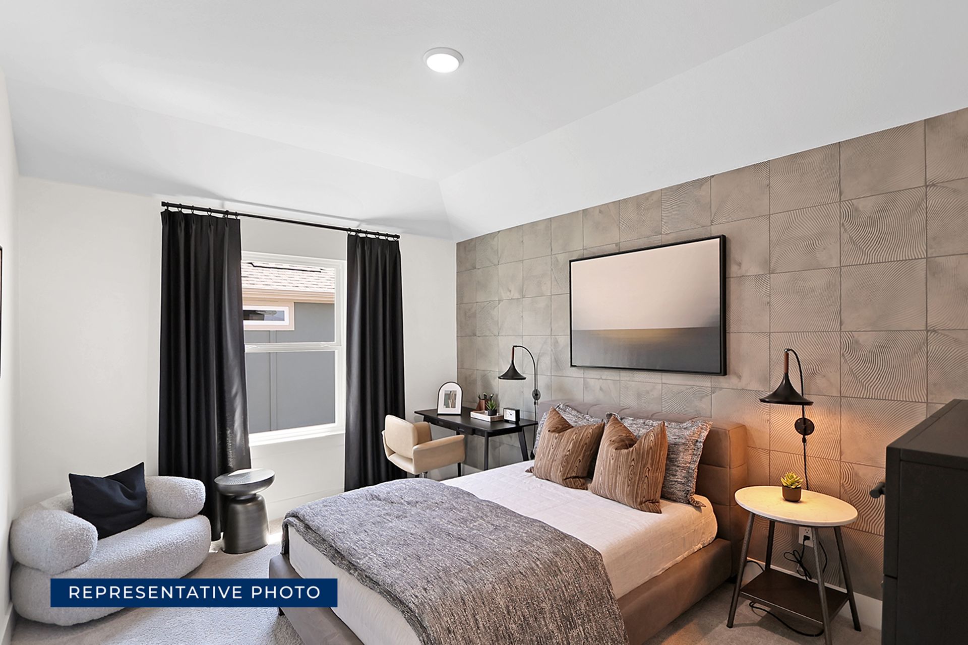 Modern bedroom with cozy seating, desk, and decorative accent wall.
