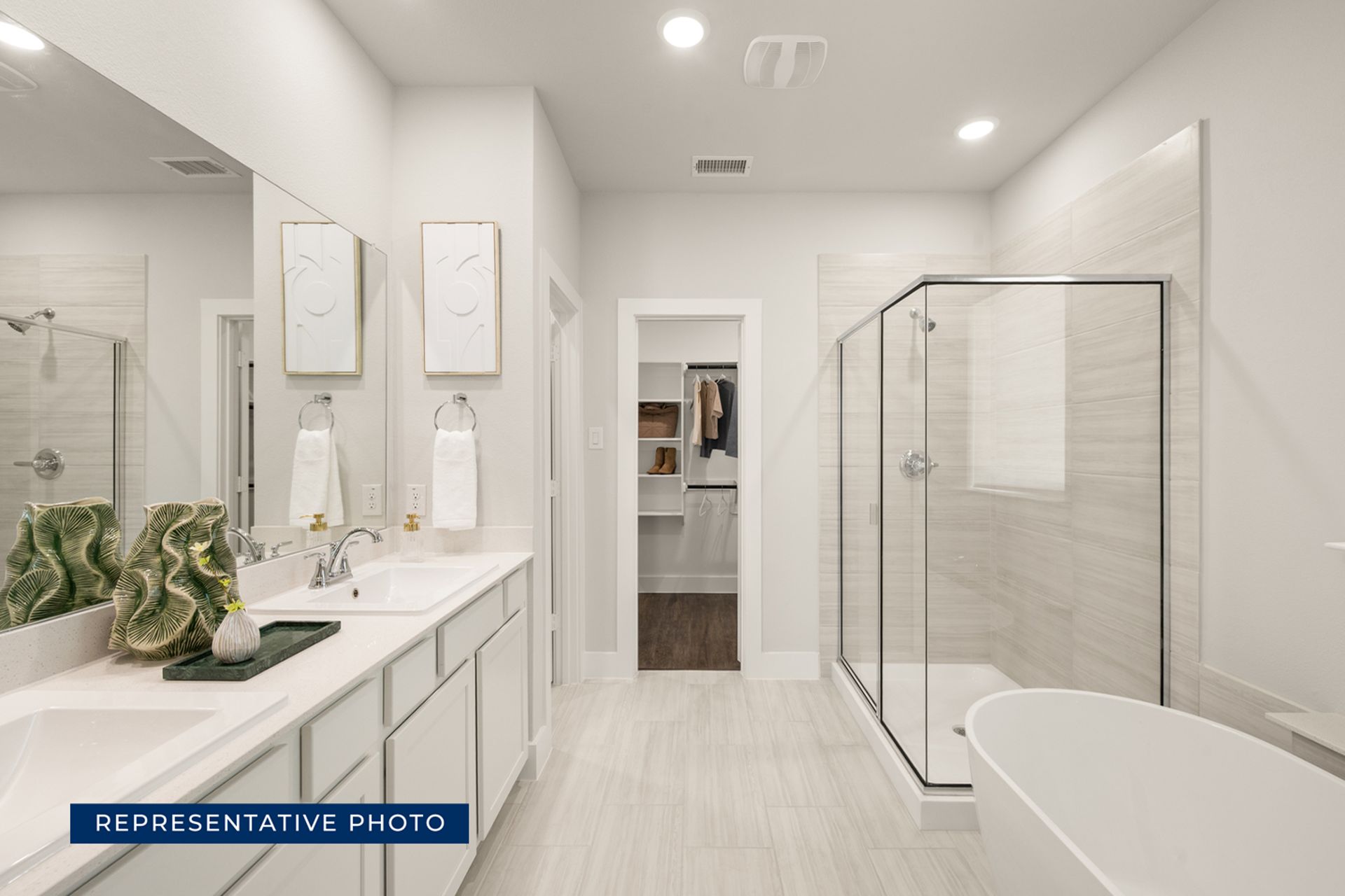 Modern bathroom with glass shower, double sinks, and open walk-in closet.