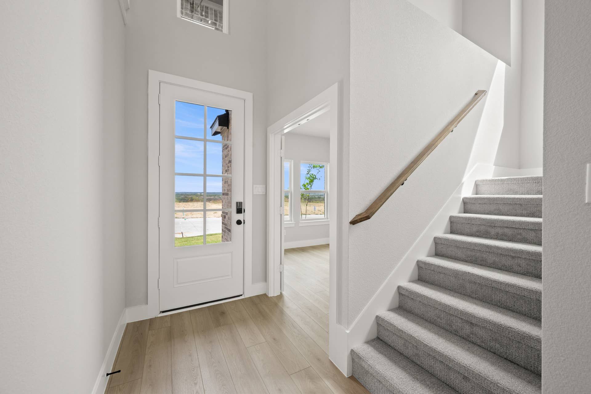 Modern entryway with glass door, light wood flooring, and carpeted stairs.