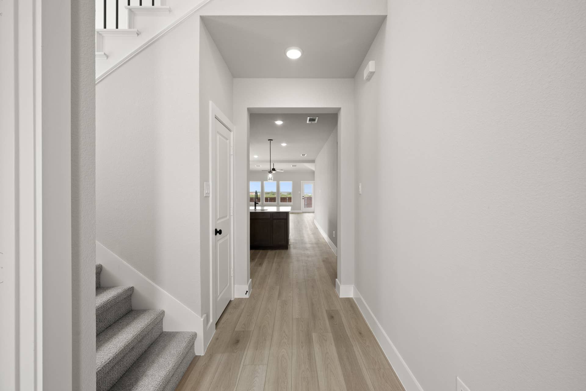Bright modern entryway with wood flooring and staircase leading to open kitchen.