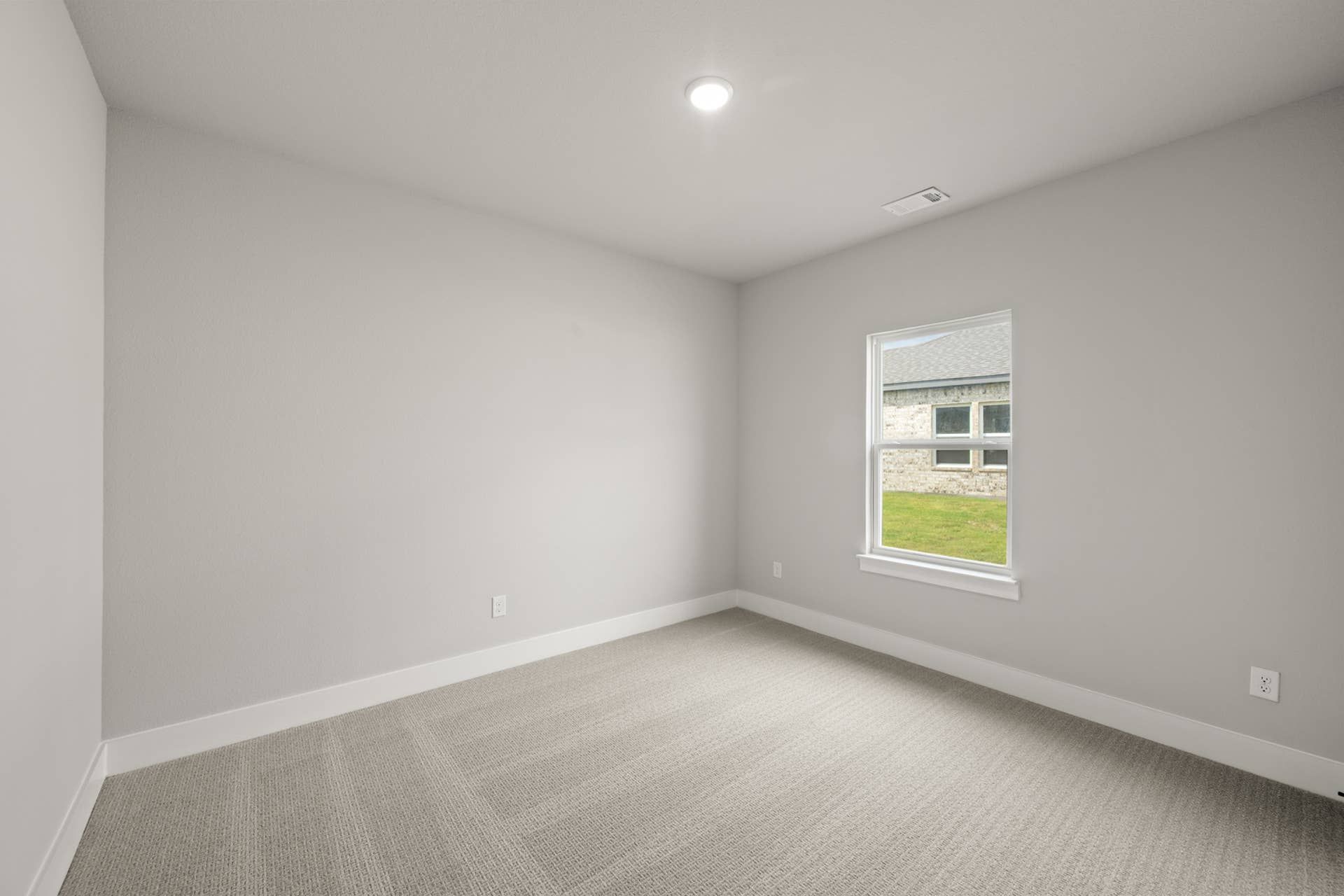 Empty bedroom with beige carpet, gray walls, and a window view.