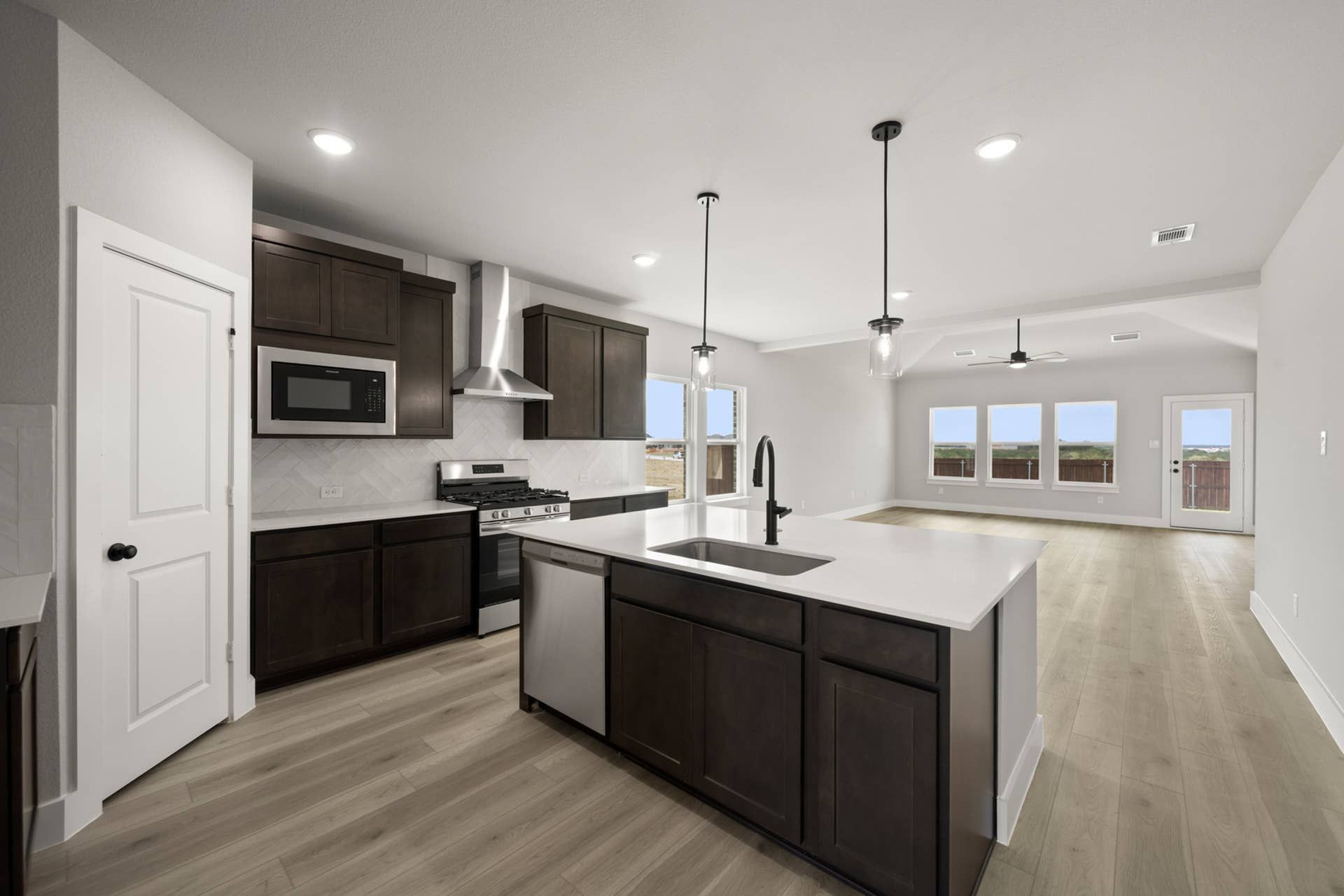 Modern kitchen with dark cabinets, island, and open living area.