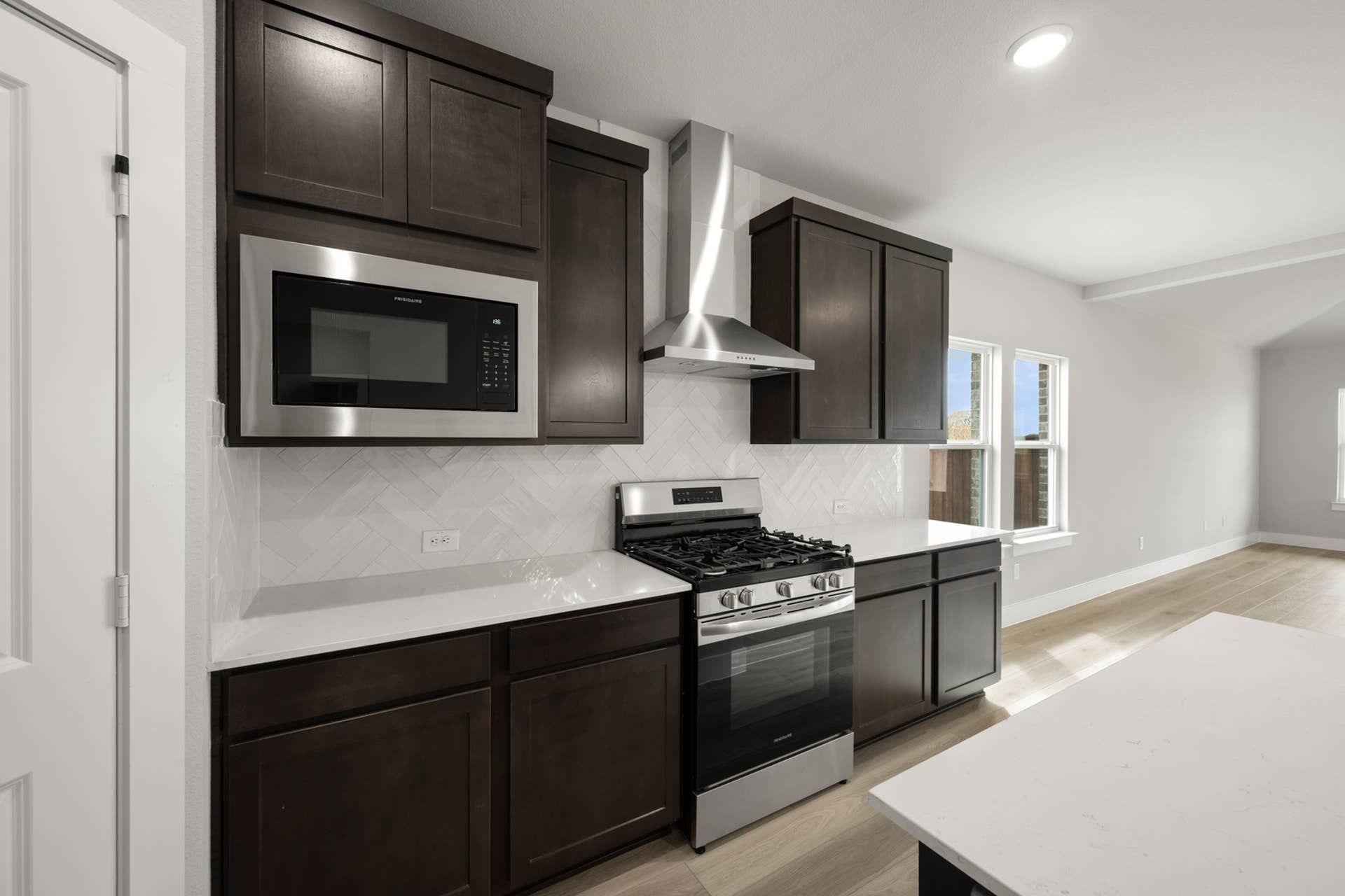 Modern kitchen with dark cabinets, stainless steel appliances, and herringbone tile backsplash.