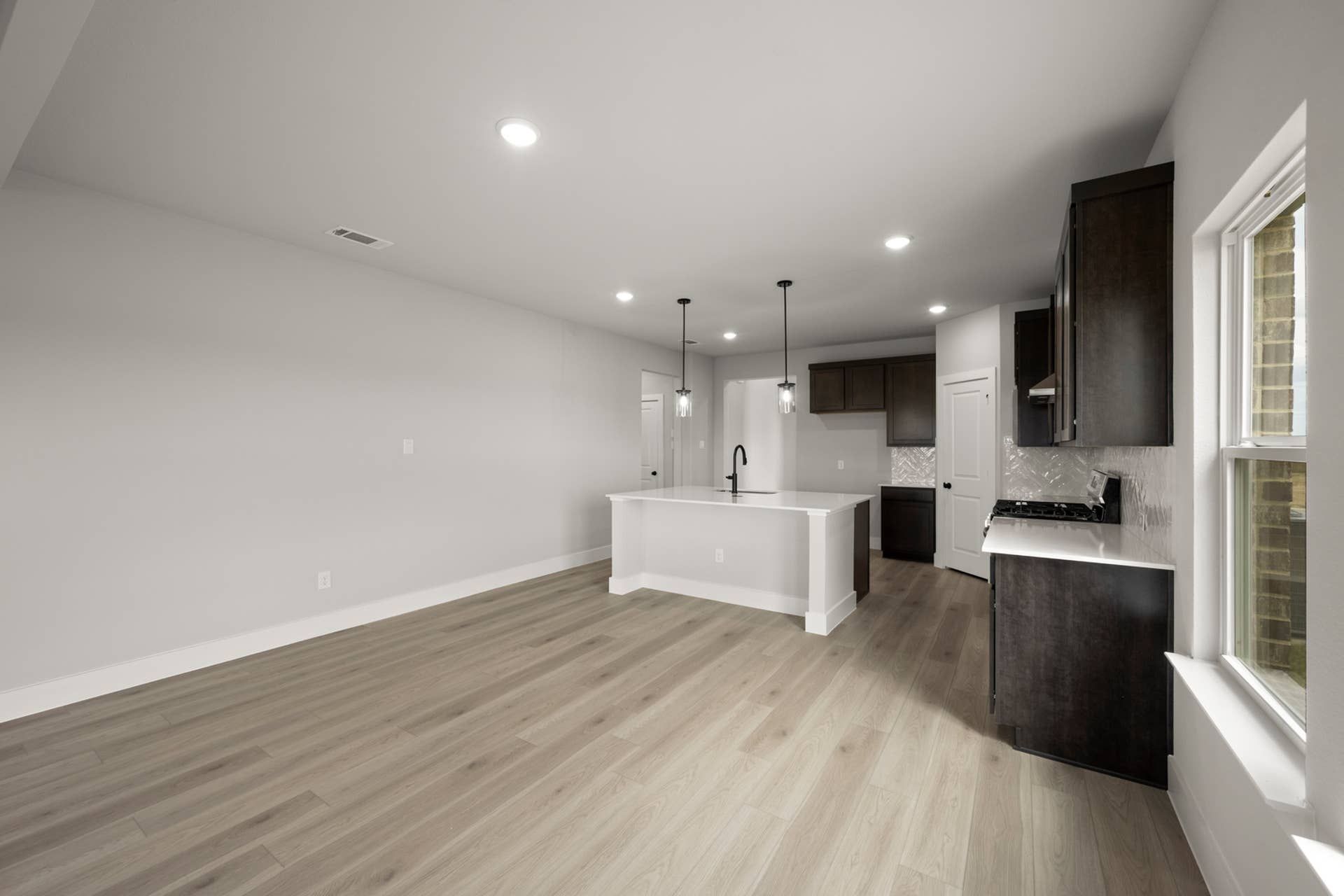 Modern kitchen with white island, dark cabinets, and wood flooring.