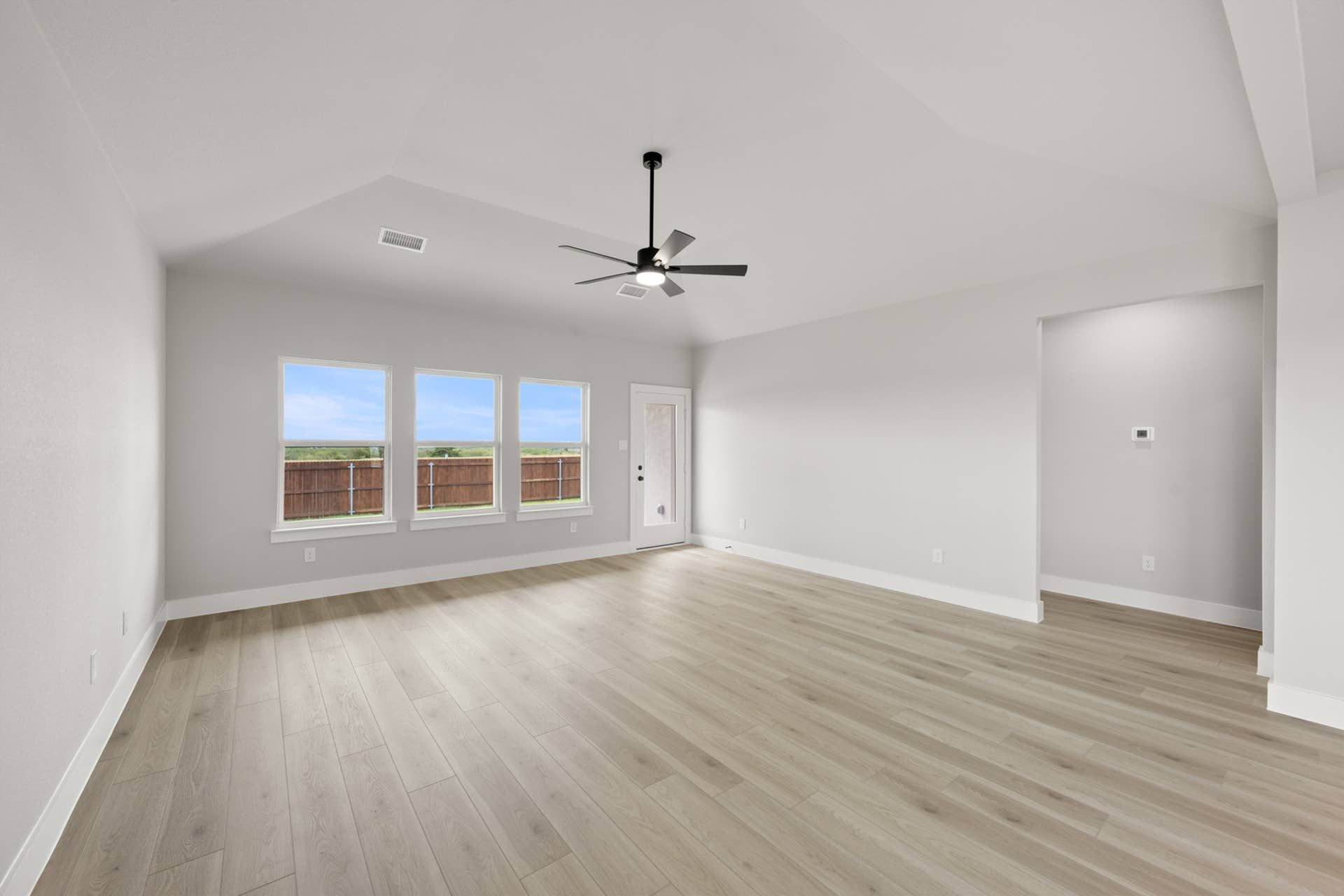 Spacious living room with light wood flooring and large windows.