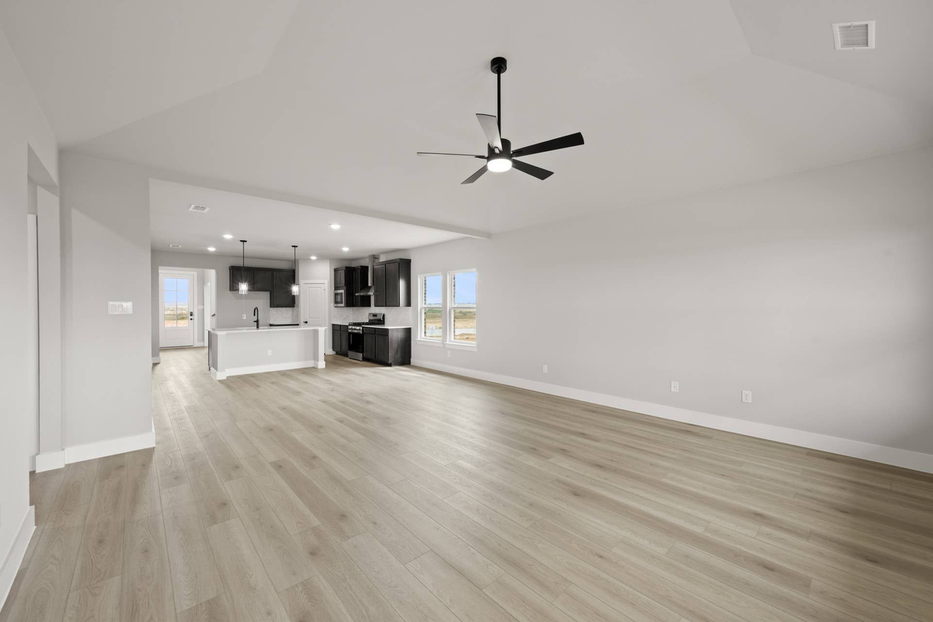 Spacious living room with open kitchen, modern ceiling fan, and light wood flooring.