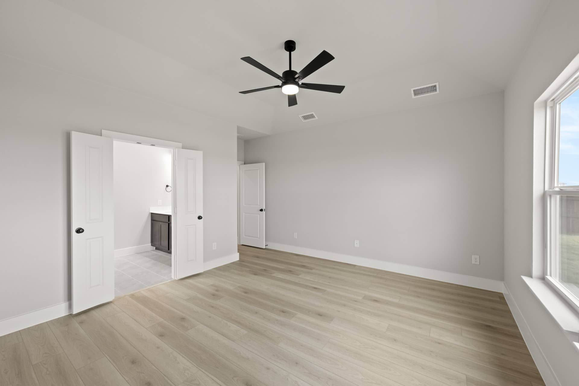 Spacious primary suite with light wood flooring and modern ceiling fan.