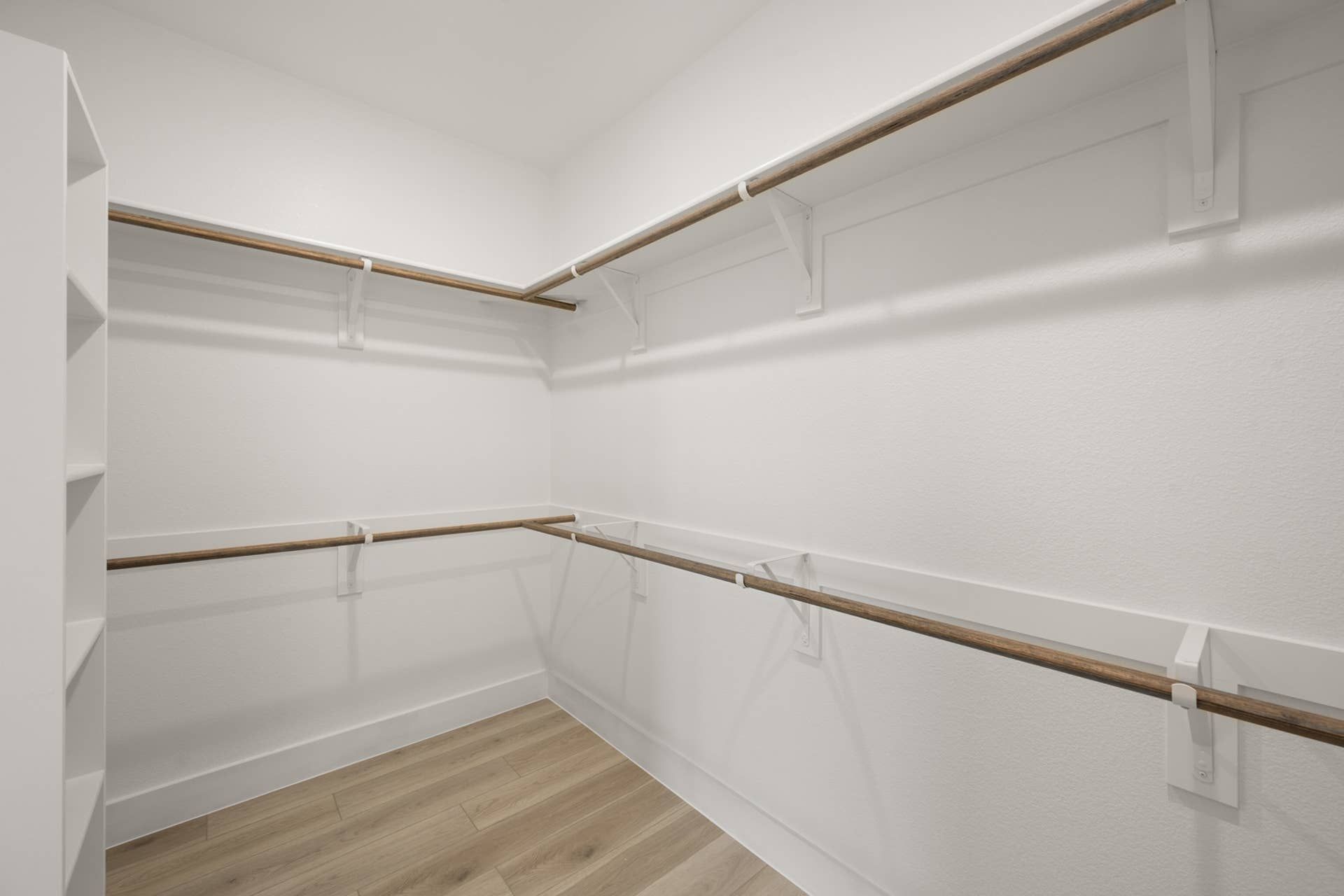 Spacious walk-in closet with wooden rods and white shelving.