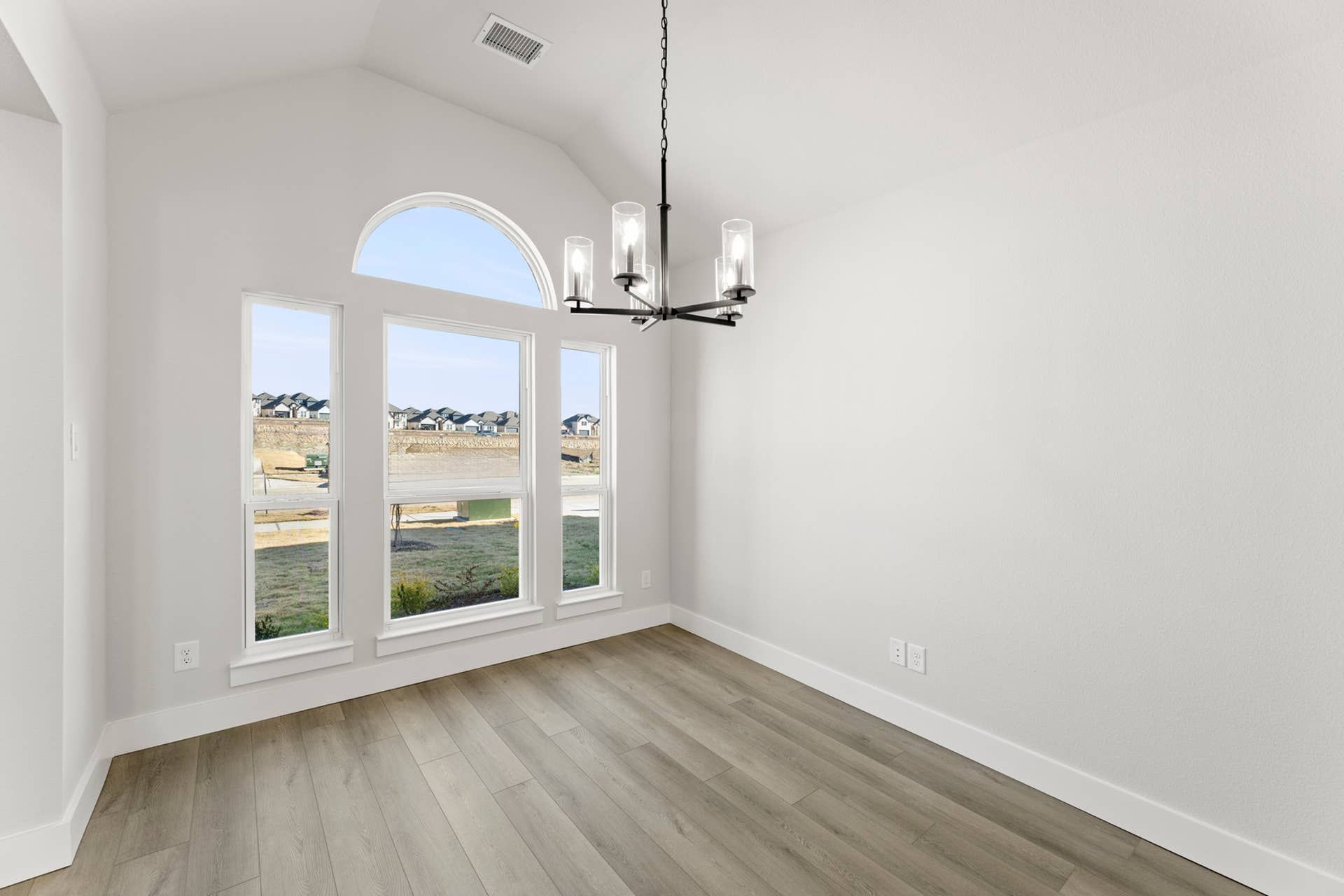 Bright dining room with large arched window and modern chandelier.