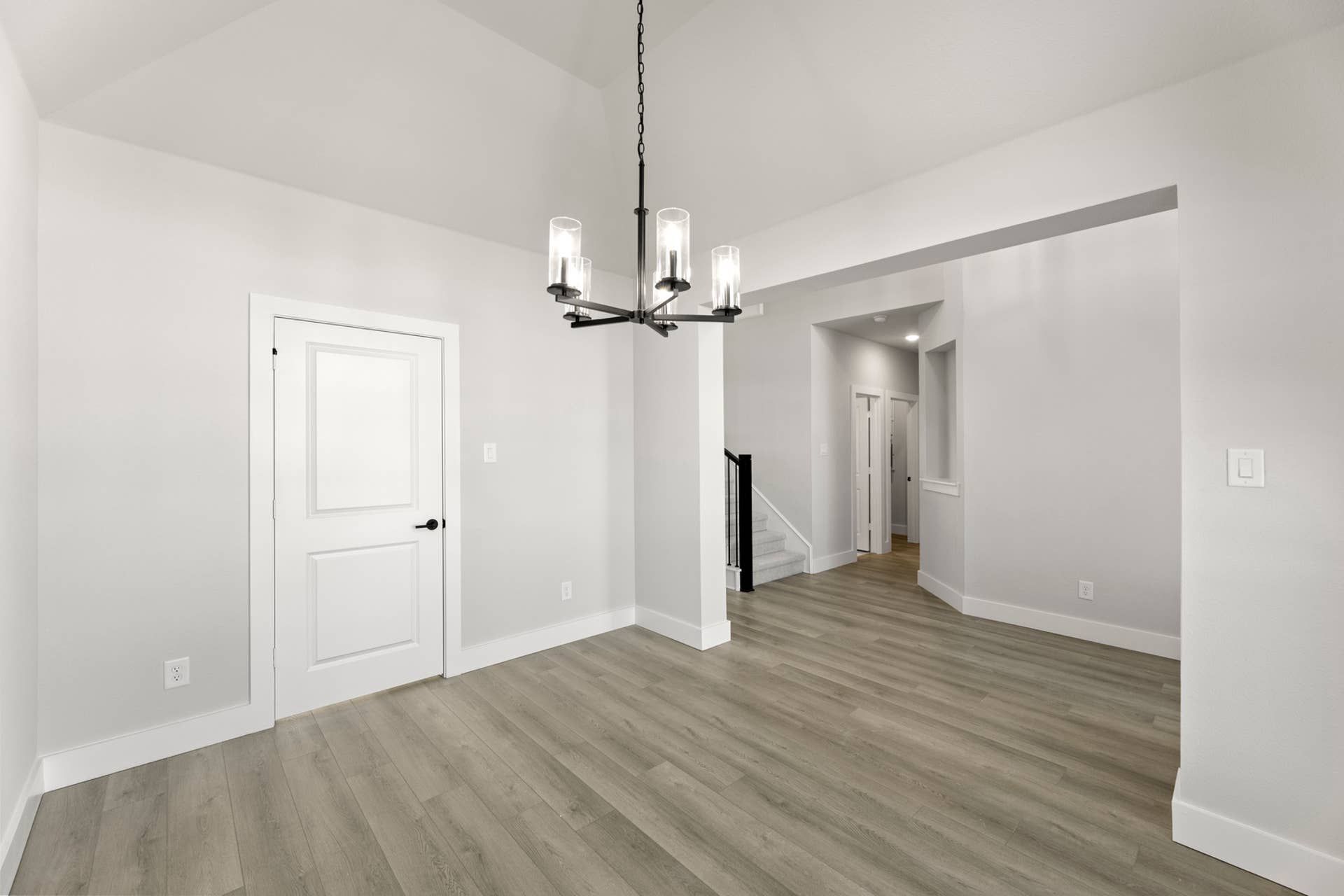 Modern dining room with chandelier, light gray walls, and wood flooring.