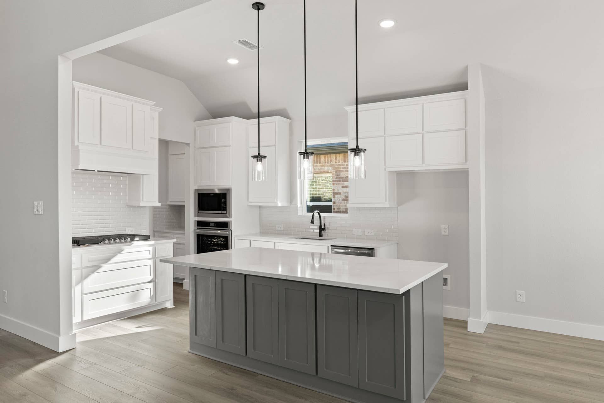 Modern kitchen with white cabinets, island, pendant lights, and hardwood floors.