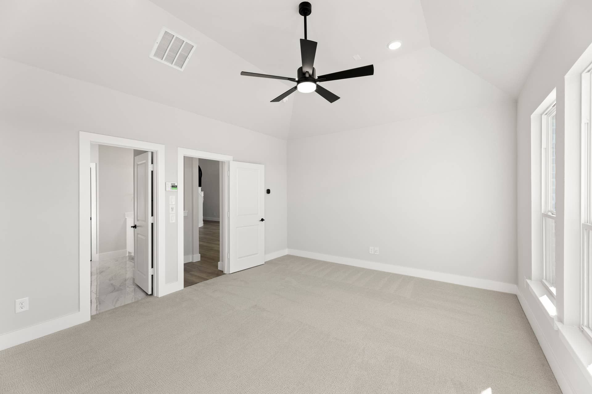 Spacious primary bedroom with ceiling fan and large windows.