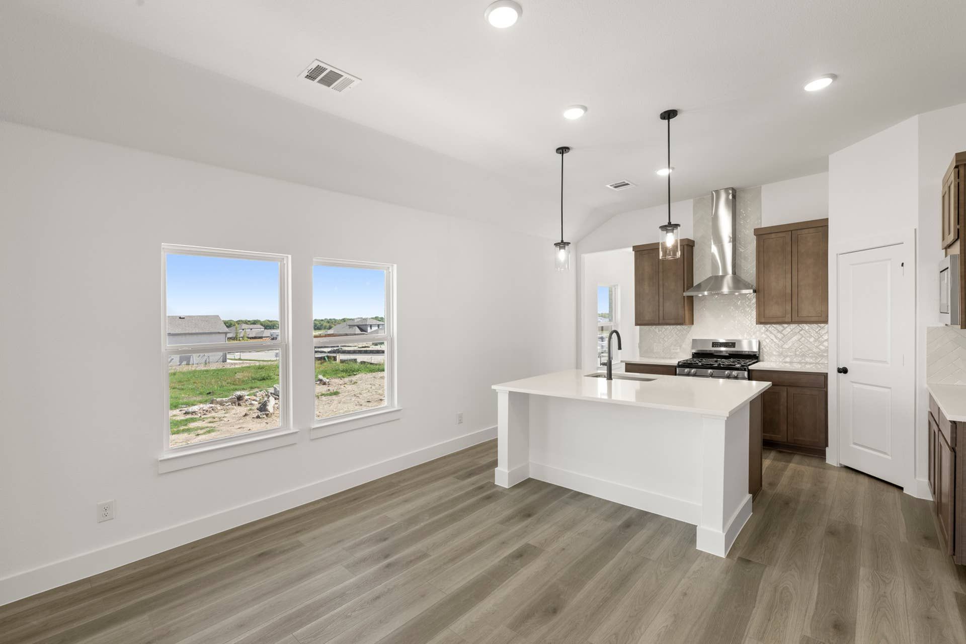 Modern kitchen with island, pendant lighting, and large windows overlooking backyard.