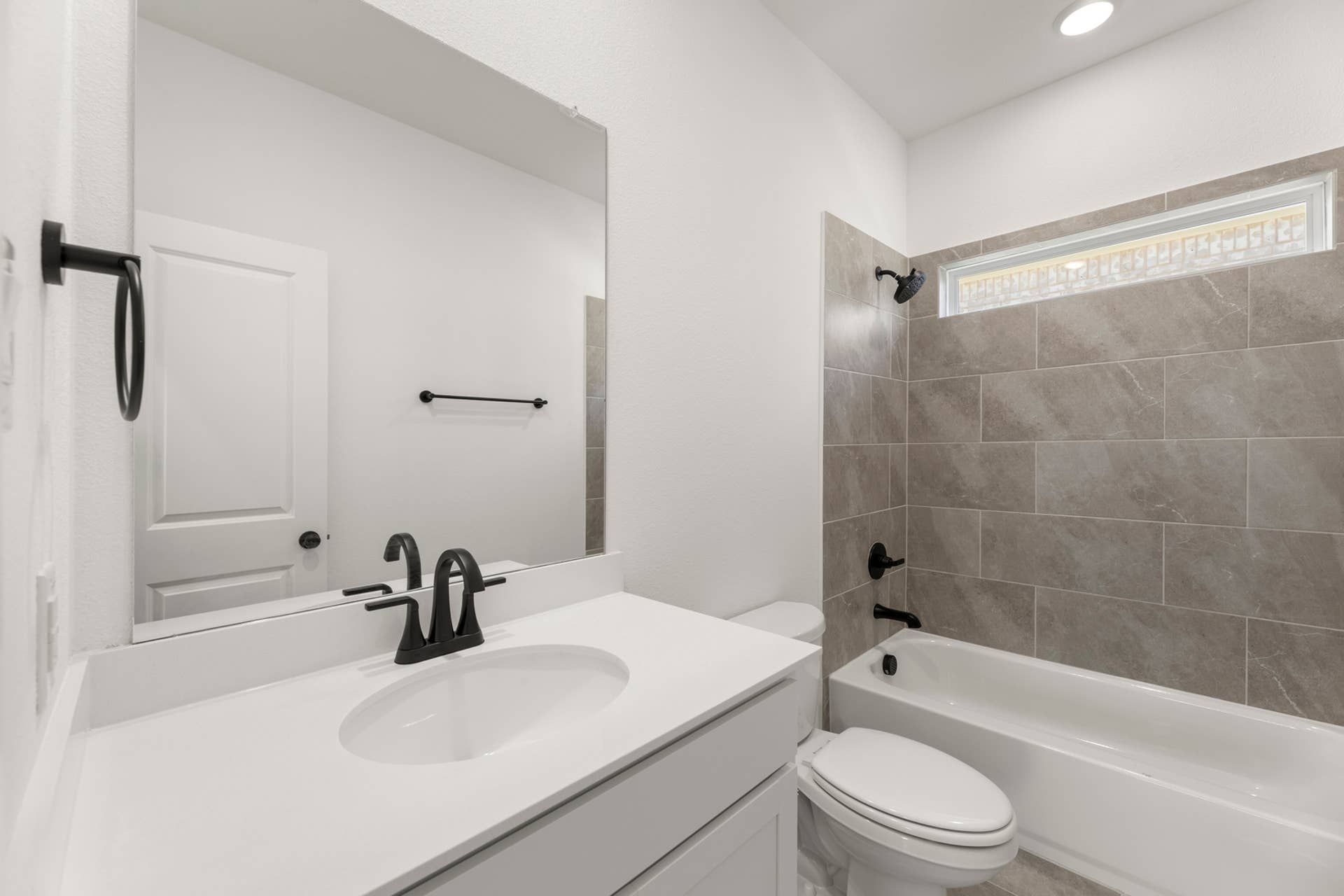 Modern bathroom with white vanity, black fixtures, and tiled shower-tub combination.