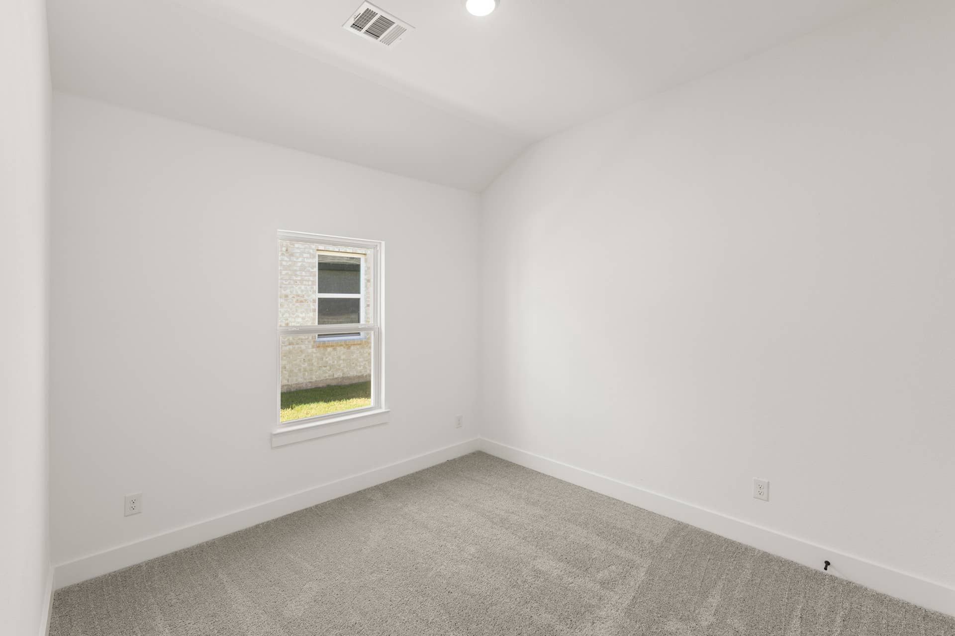 Bright empty bedroom with single window and gray carpet flooring.