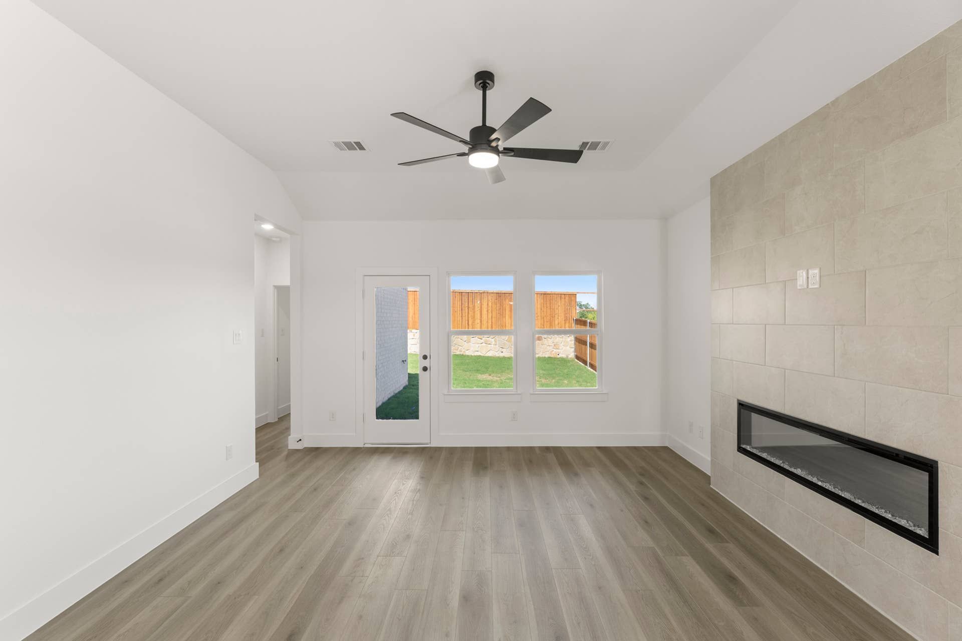Modern living room with ceiling fan, sleek fireplace, and large windows.
