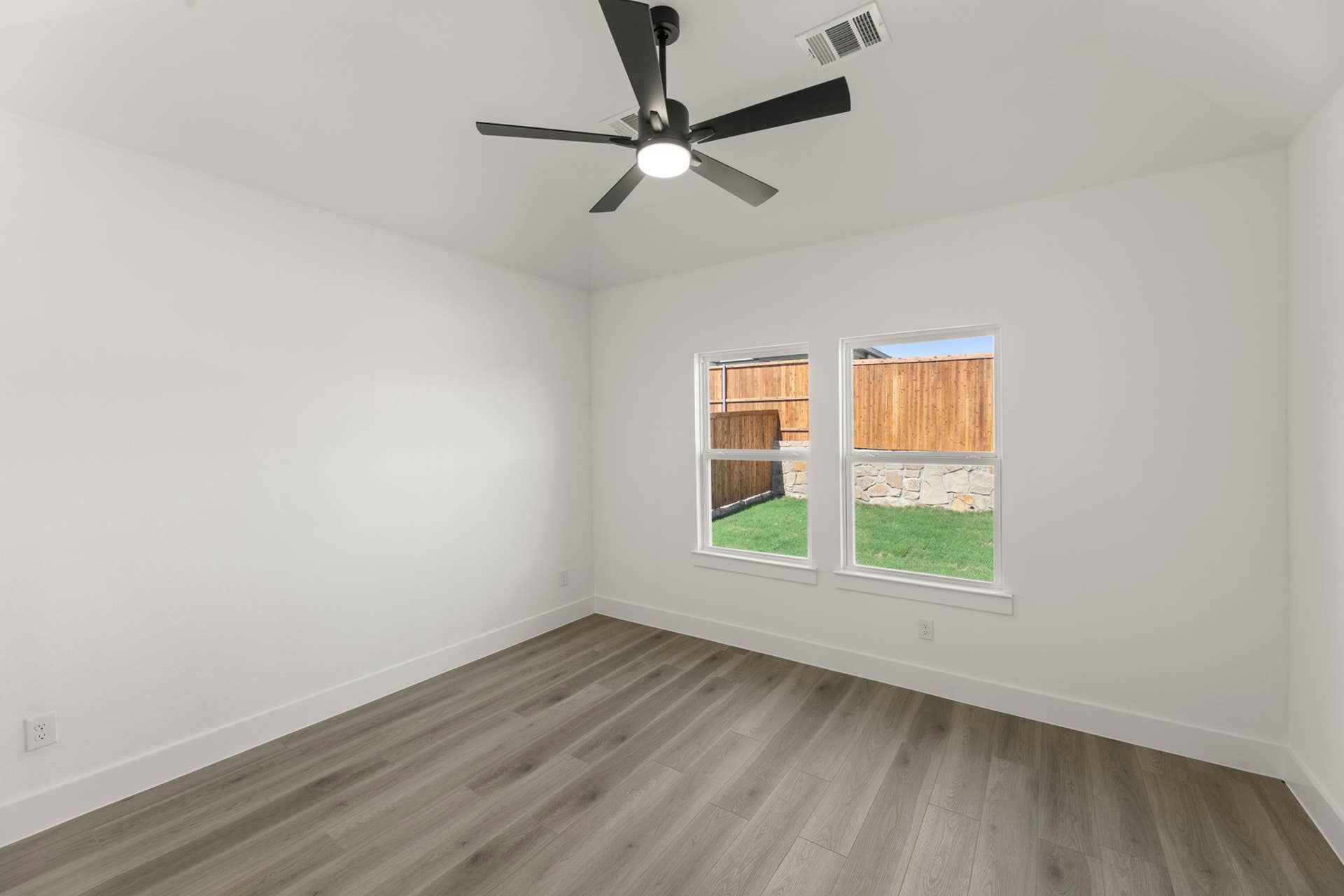 Spacious room with hardwood floors, ceiling fan, and large windows overlooking backyard.