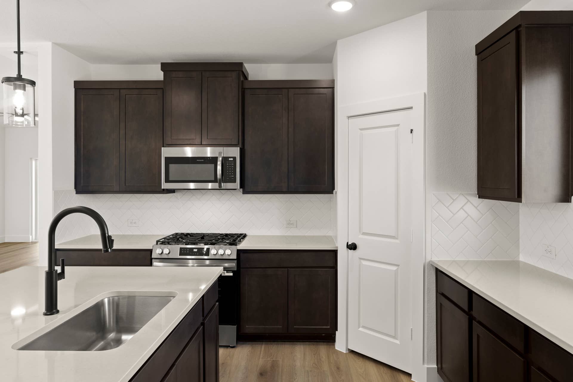 Modern kitchen with dark cabinets, stainless steel appliances, and herringbone backsplash.