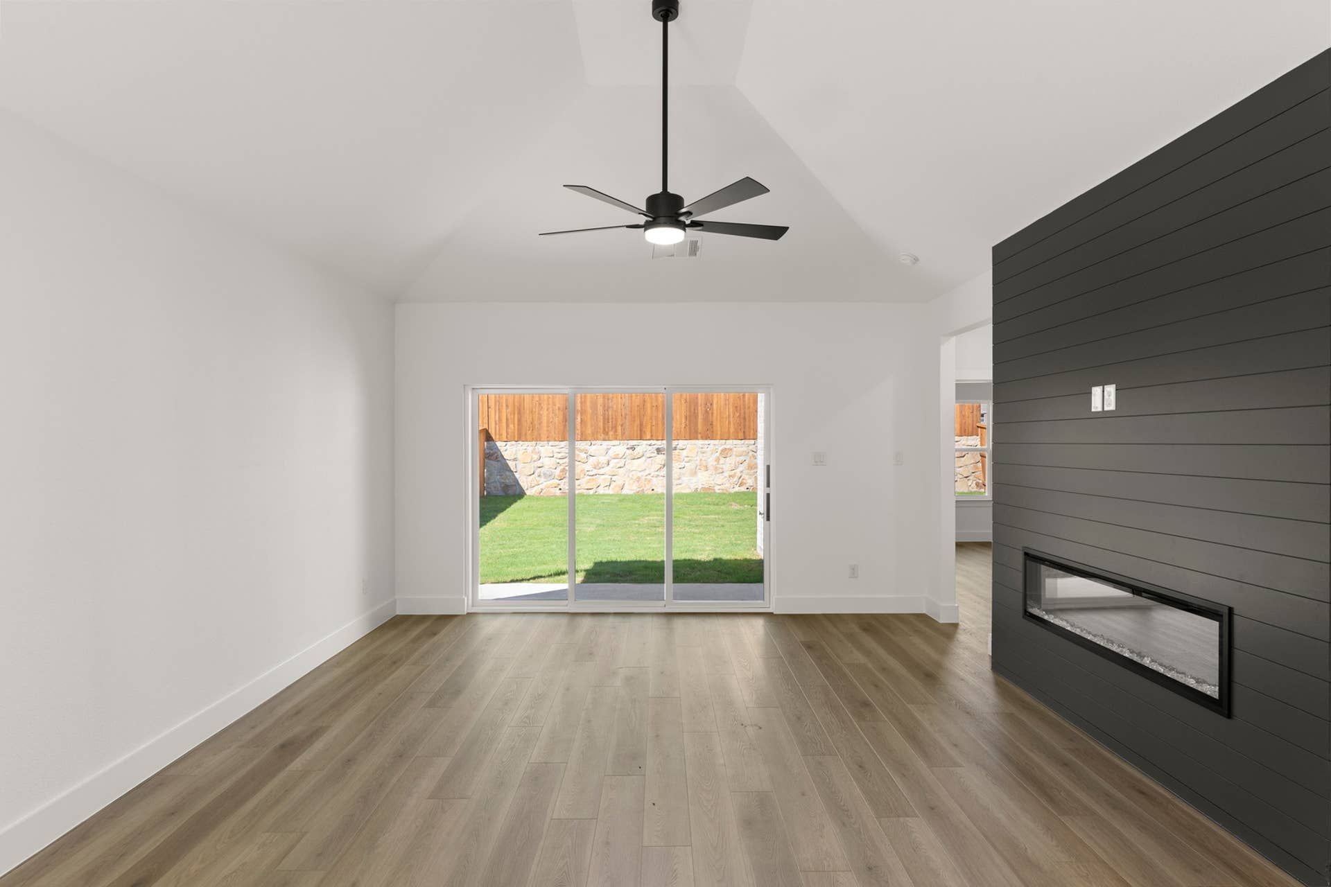 Modern interior with sliding glass doors, wood flooring, and dark shiplap fireplace.