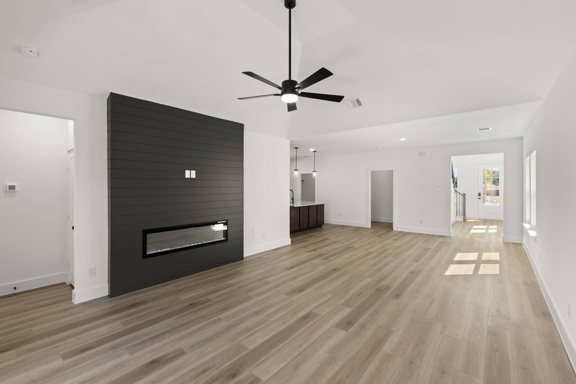 Modern living room with wood floors, black accent wall, and ceiling fan.