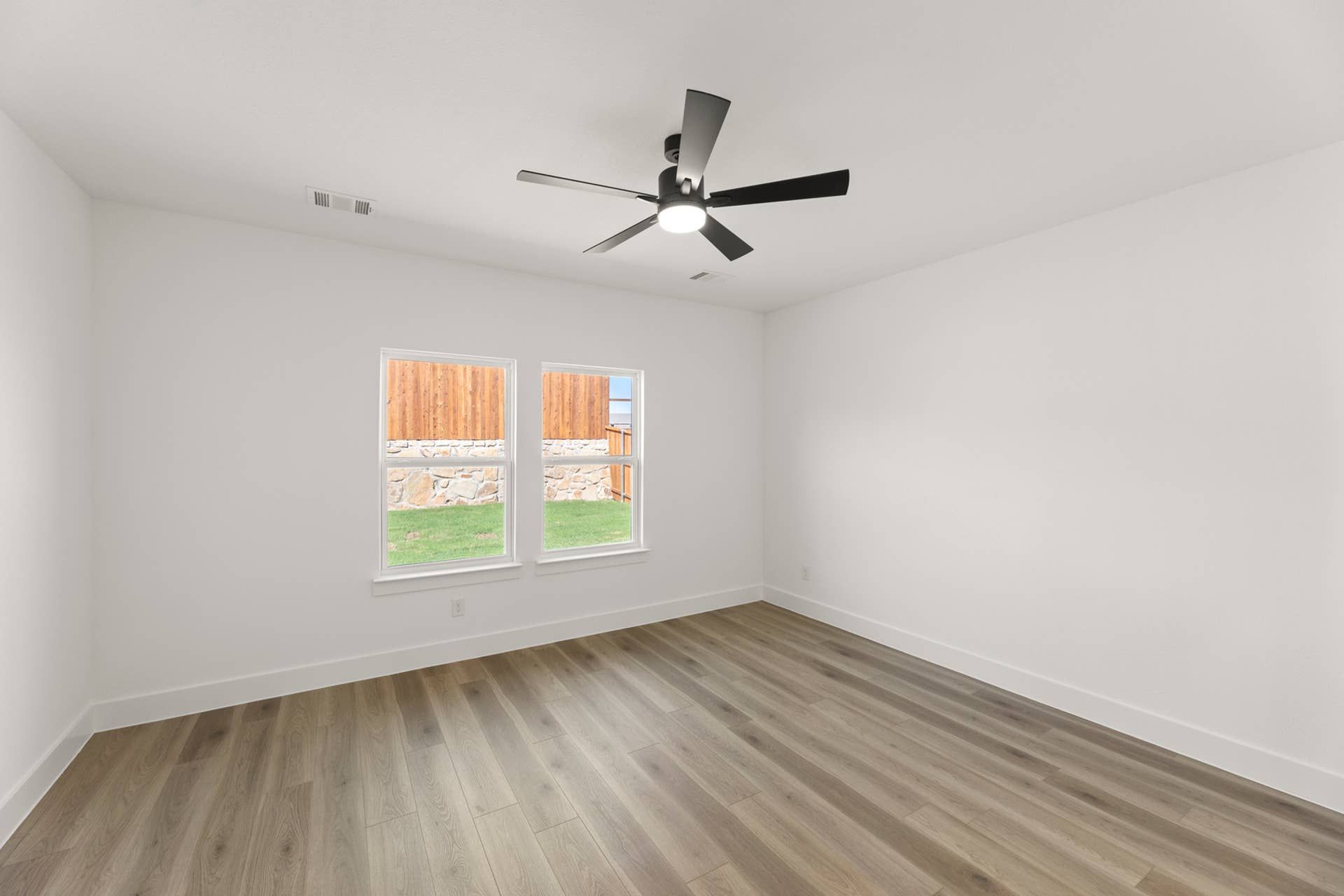 Bright empty room with wood flooring and ceiling fan.