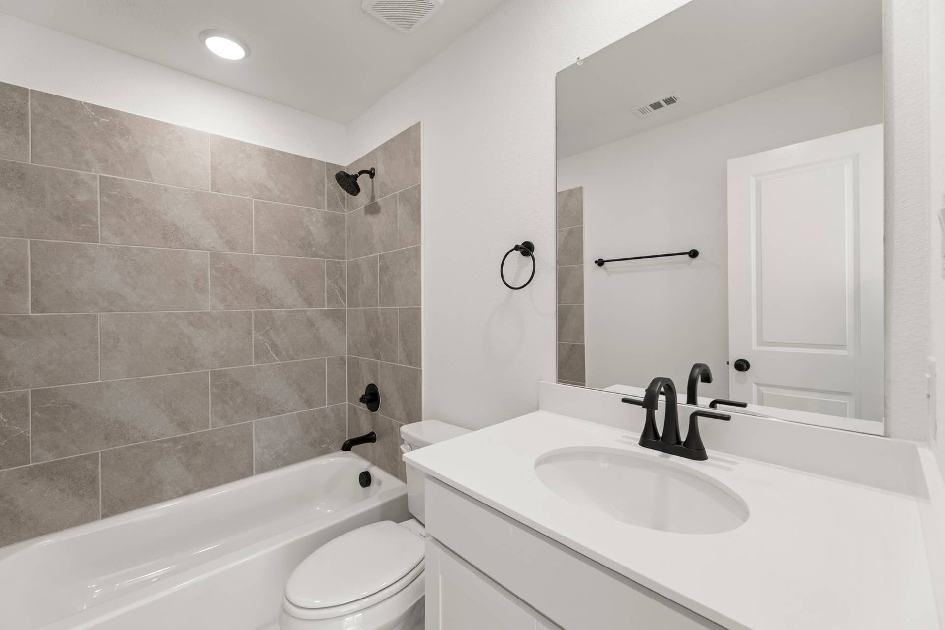 Modern bathroom with white vanity, black fixtures, and tiled bathtub surround.
