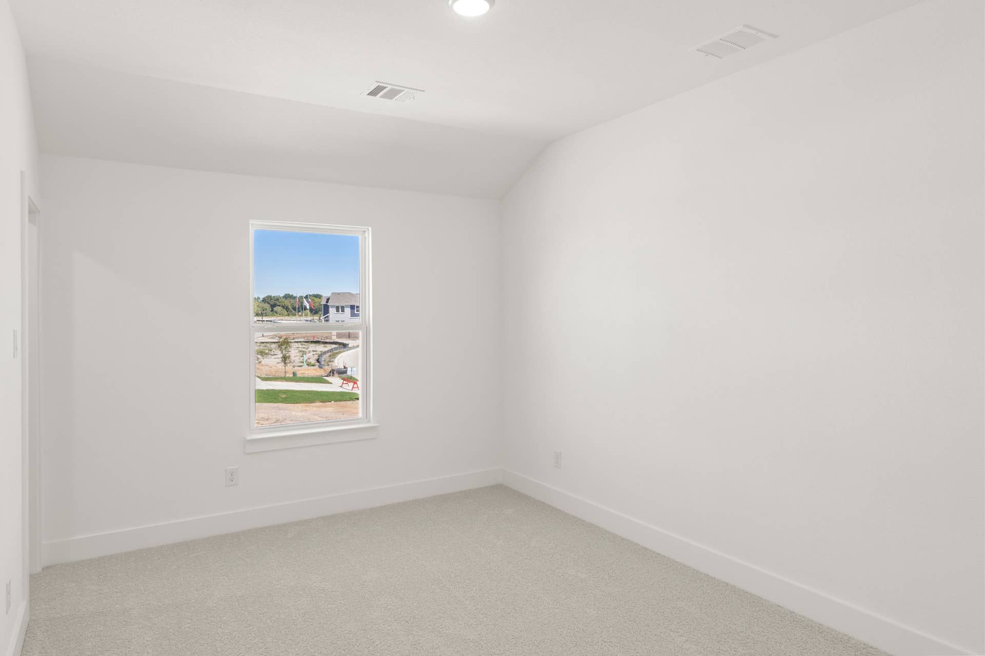 Bright, empty bedroom with carpet and a single window view of suburban neighborhood.