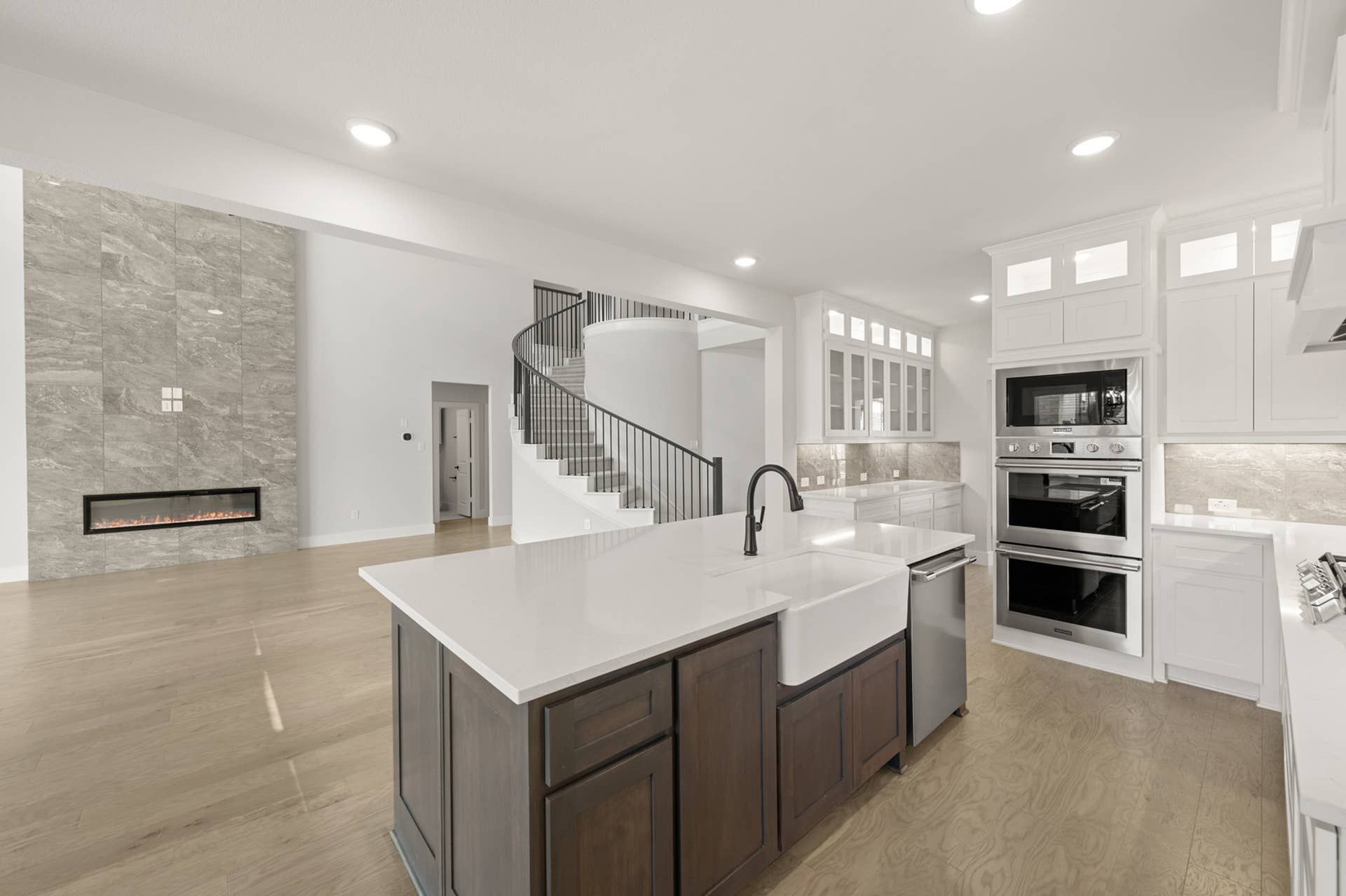 Modern kitchen with island, spiral staircase, and stone fireplace in open-plan design.