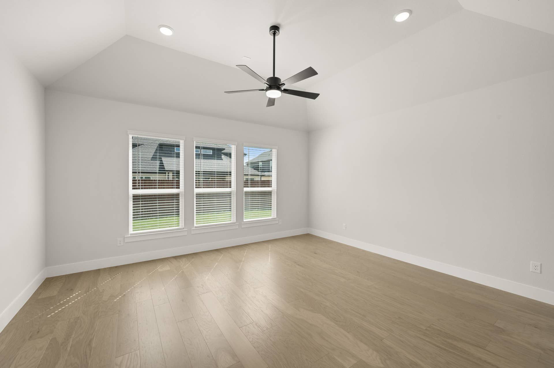 Spacious primary suite with wood flooring and ceiling fan, featuring large windows.