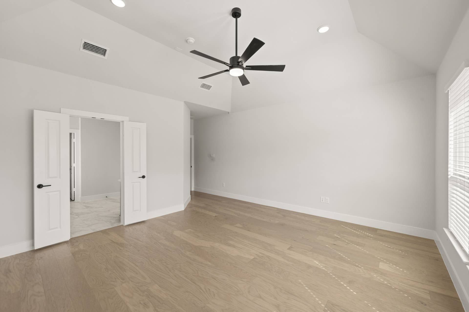 Spacious primary suite with hardwood floors, ceiling fan, and double doors to bathroom.