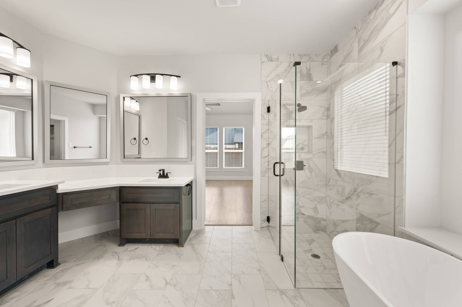 Luxurious bathroom with marble tile, glass shower, and dual vanity mirrors.