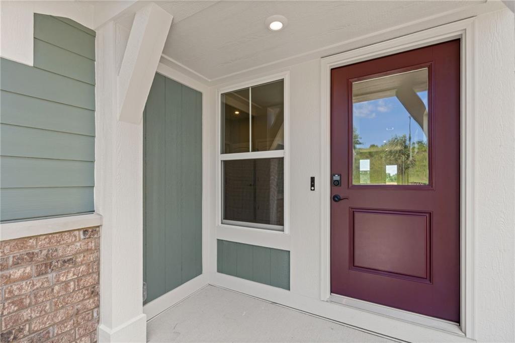 Entryway featuring a rich maroon door with glass insert, recessed lighting, brick detailing, and a smart lock system