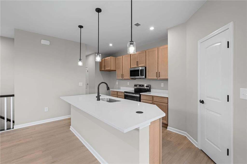 Modern kitchen featuring wood-finish flooring, light-toned cabinetry, stainless steel appliances, and an island with a white countertop and sink