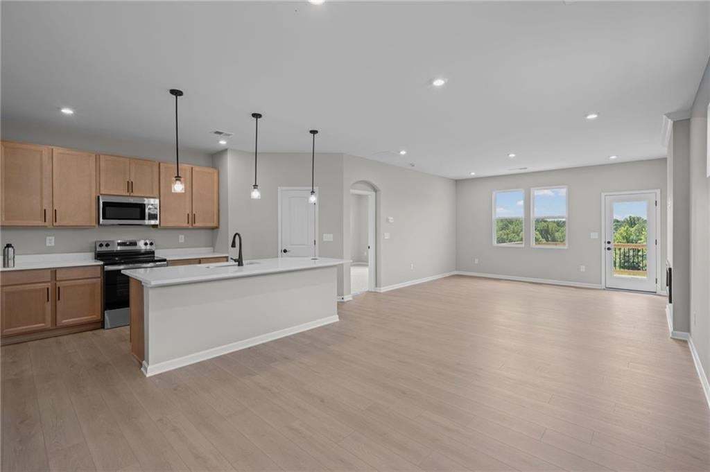 Open-concept living and dining area with wood-finish flooring throughout, pendant lighting, and abundant natural light from multiple windows and glass doors