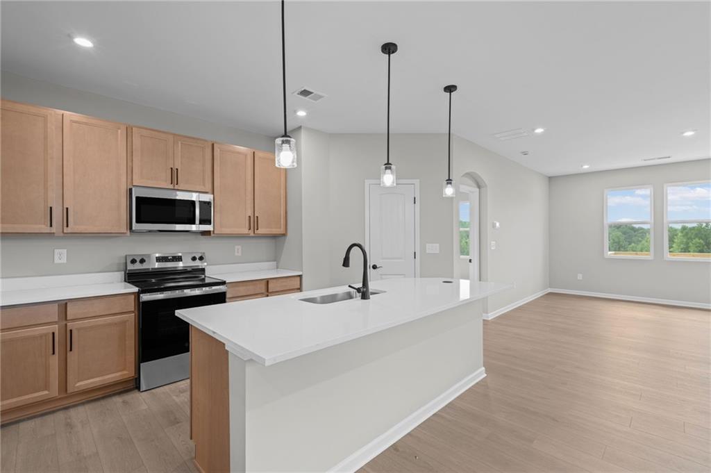 Kitchen featuring light wood-finish cabinetry, stainless steel appliances, a center island with integrated sink, and pendant lighting