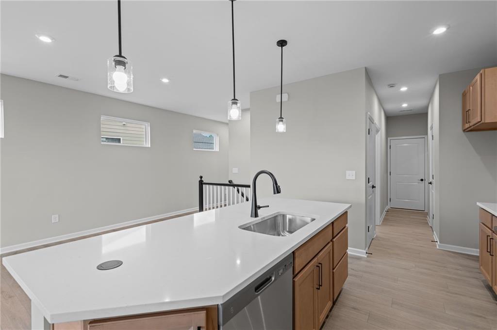 Kitchen island with a white countertop and integrated sink, stainless steel dishwasher, pendant lighting, and wood-finish flooring