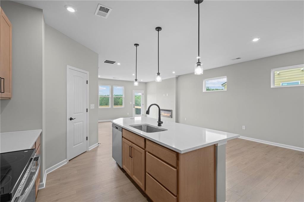 Kitchen island with integrated sink, stainless steel dishwasher, pendant lighting, and light wood-finish flooring