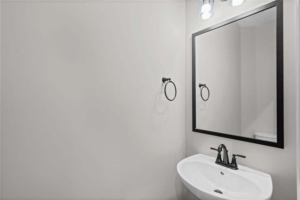 Modern bathroom featuring a curved white porcelain sink with matte black widespread faucet, framed mirror with black metal trim, and clean white walls with recessed ceiling lighting