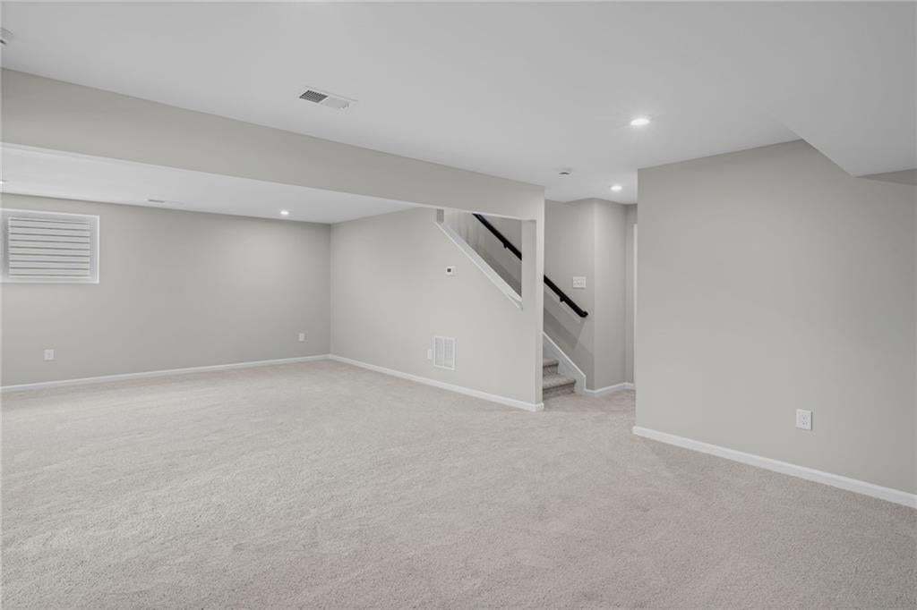 Expansive carpeted area with recessed lighting, light gray wall finishes, and a staircase with dark handrails