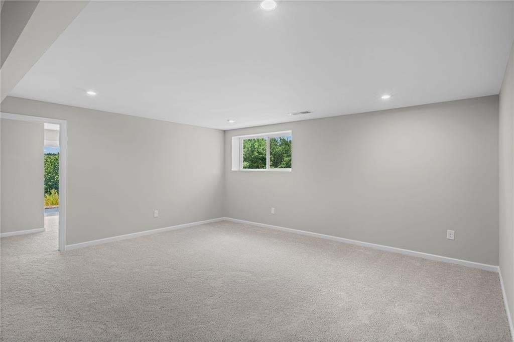 Recessed lighting illuminates a spacious room featuring light-colored carpeting, a window, and a wide entryway