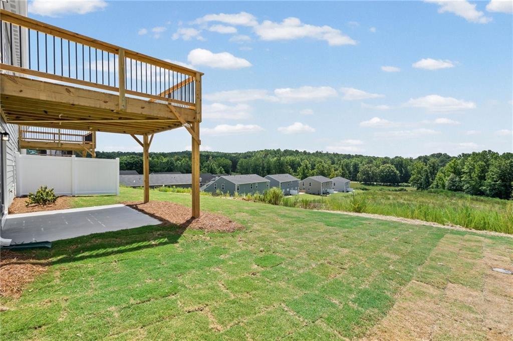 Upper-level wood deck with black balusters, ground-level patio, spacious grass area, and a white privacy fence