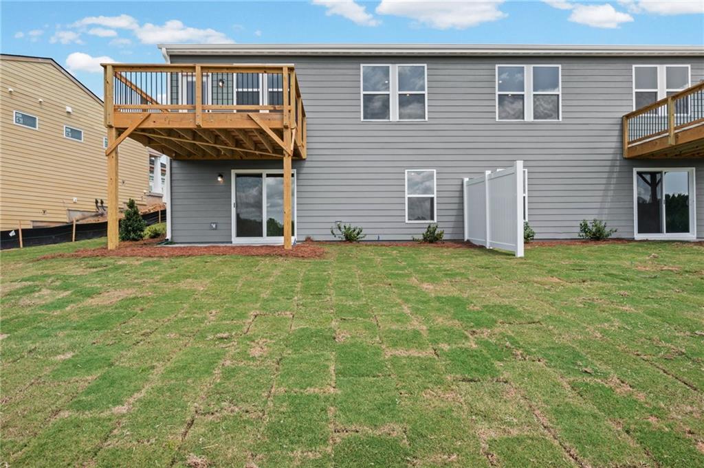 Rear exterior with grey siding, multiple windows, and a wood-finish deck with black railings