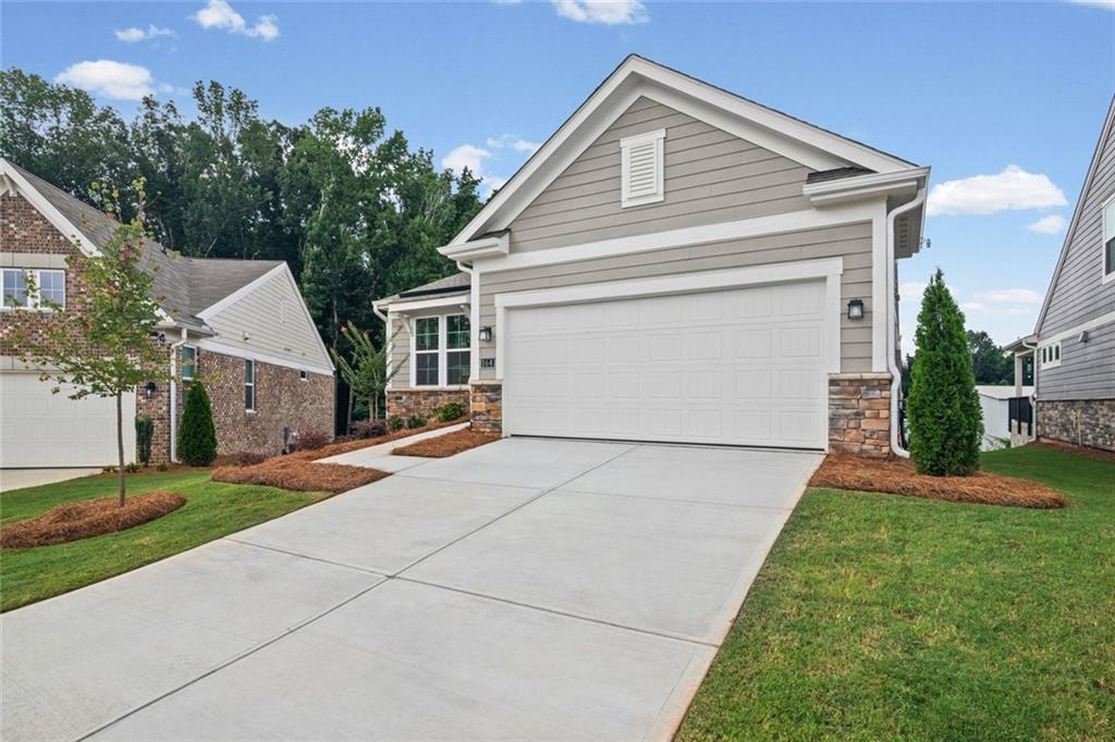 Contemporary exterior featuring light grey siding, stone accents, a two-car garage, and a concrete driveway
